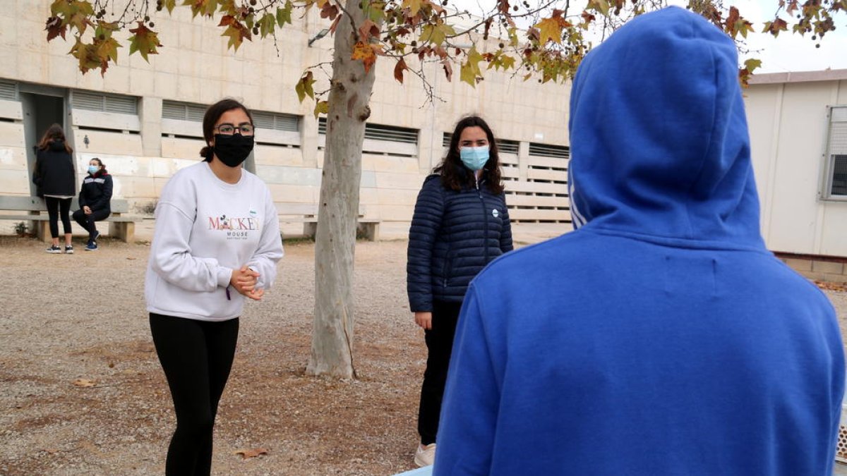 Un jove amb caputxa conversant sobre les mesures anticovid amb dues companyes de l'institut a Alcanar.