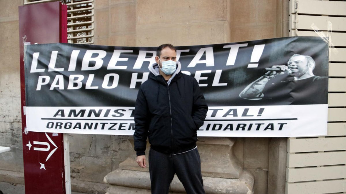 Plano abierto donde se puede ver al rapero Pablo Hasél delante de una pancarta que pide su libertad.