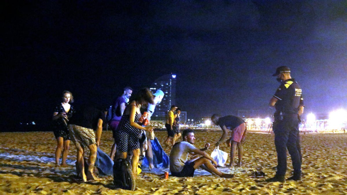Un grup de persones que feia el 'botellón' a la platja de la Barceloneta de Barcelona s'aixequen davant la presència d'una línia d'agents de la Guàrdia Urbana abans de marxar, a quarts d'una de la matinada.