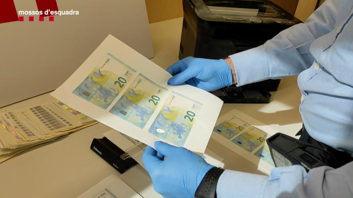 Un agente dels Mossos d'Esquadra sujetando billetes de 20 euros falsificados.