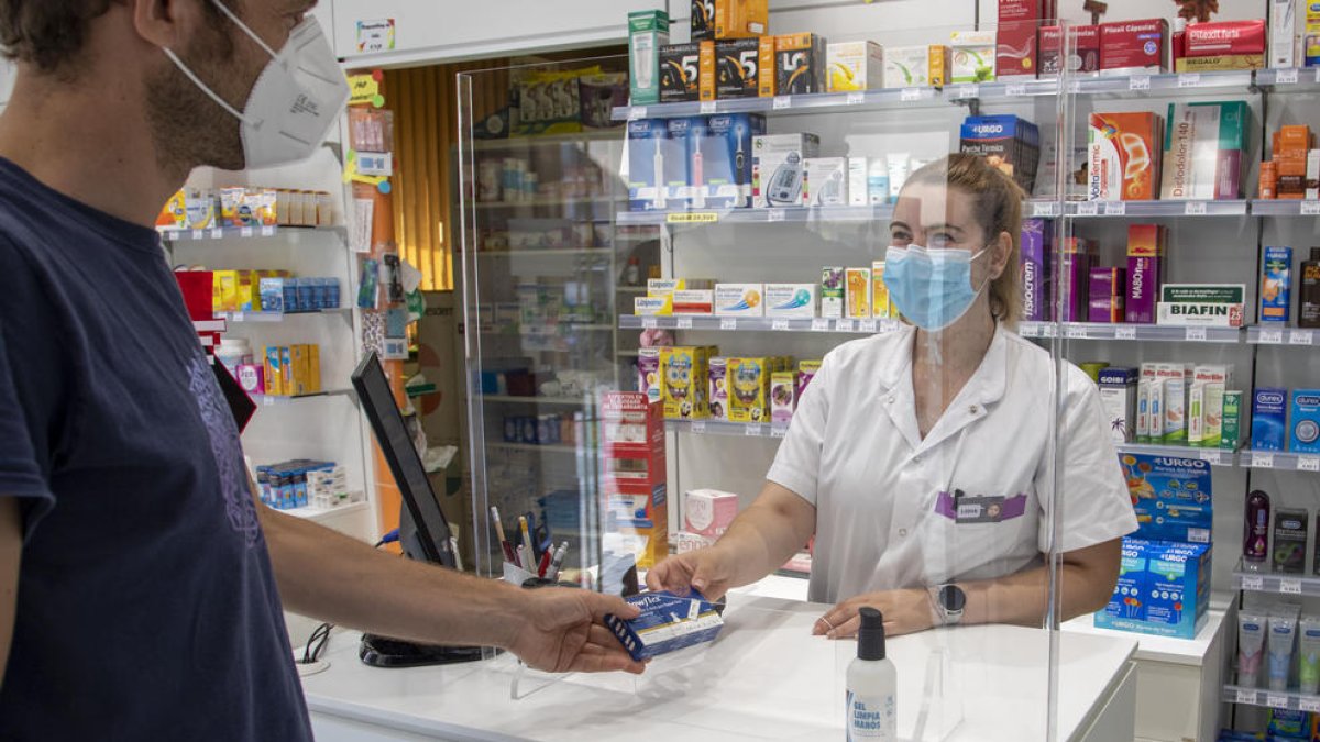Una farmacèutica de la farmàcia Salazar, al carrer Cos del Bou, entrega un test d'antígens a un client.