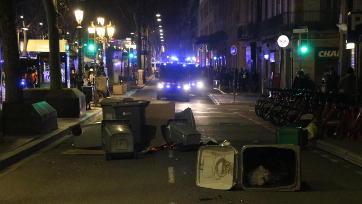 Una pequeña barricada con contenedores en la Rambla de Barcelona, con unas furgonetas de los Mossos en segundo plano.