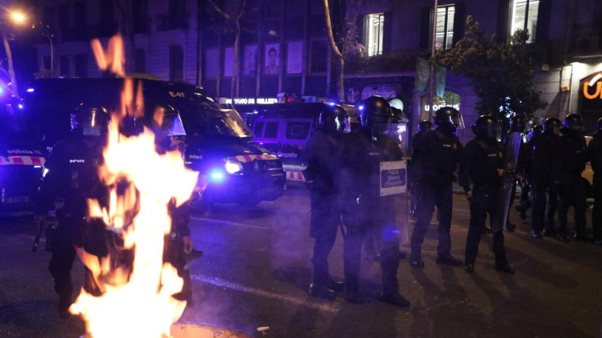 Agents dels Mossos d'Esquadra al costat d'una paperera en flames durant els aldarulls posteriors a una manifestació dels CDR pel quart aniversari de l'1-O.