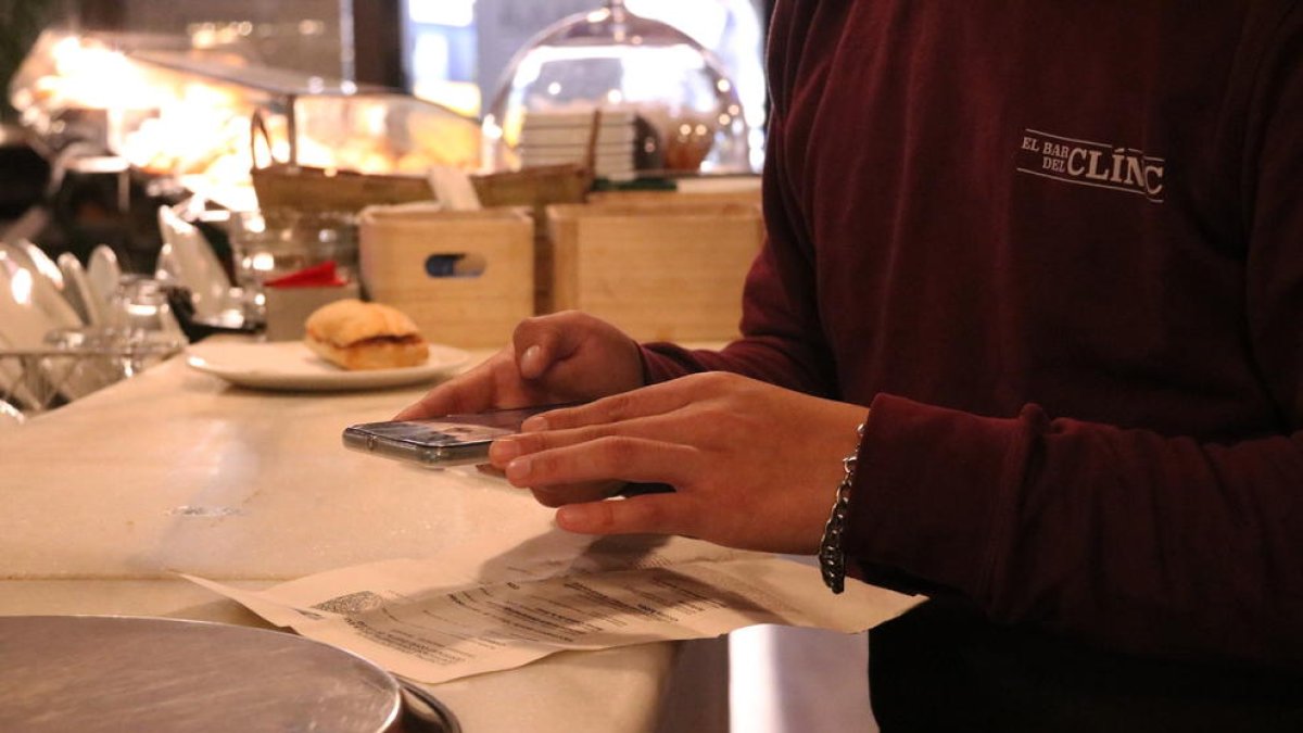 Plano corto de la mano de un camarero pidiendo el certificado covid en la entrada de un bar.