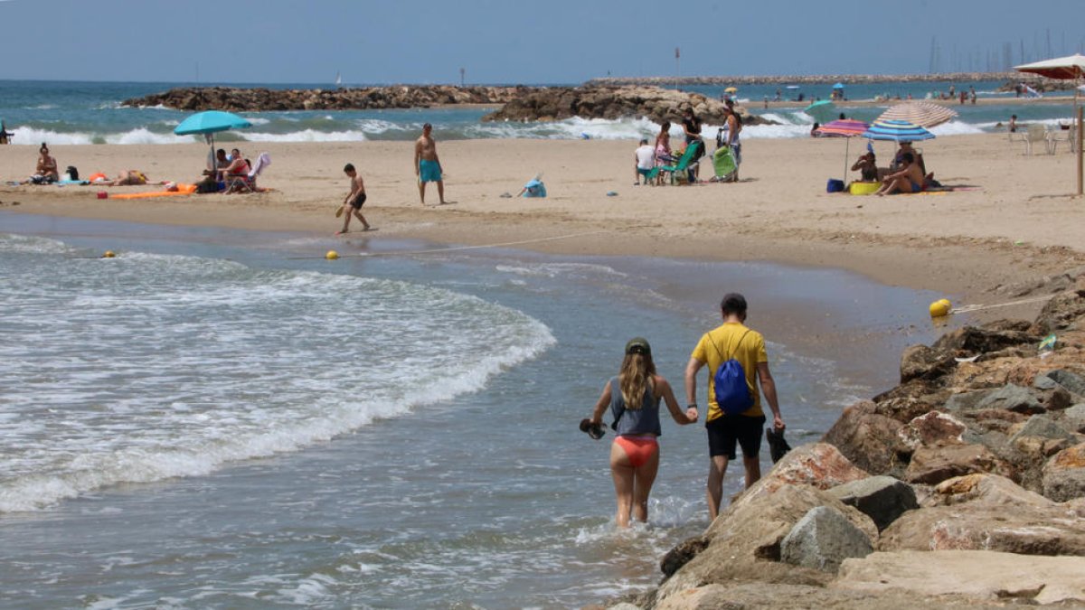 Una playa de Cunit sin arena, con dos bañistas cruzando con el agua en los tobillos.