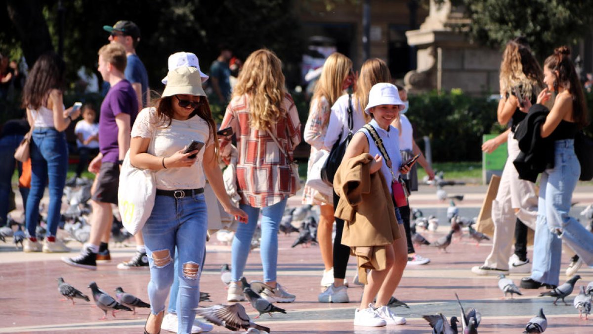 Unas turistas pasean entre palomas en la plaza de Cataluña de Barcelona.