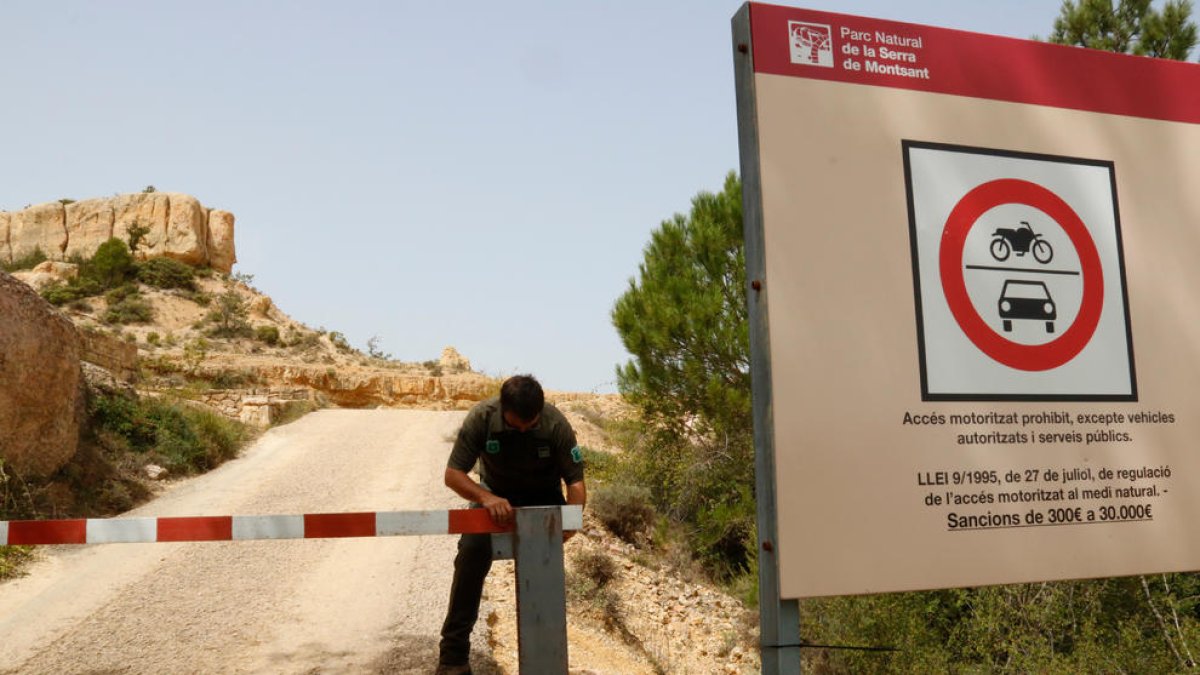 Un cartel del Parque Natural a la Sierra del Montsant con un Agente Rural poniendo la valla que prohíbe el acceso.