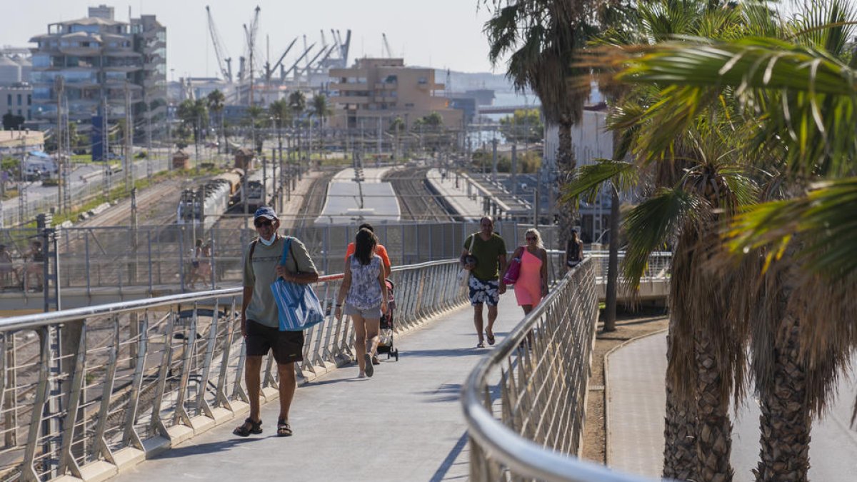 Persones creuant la passarel·la que facilita l'accés des de la Baixada del Toro fins a la platja.