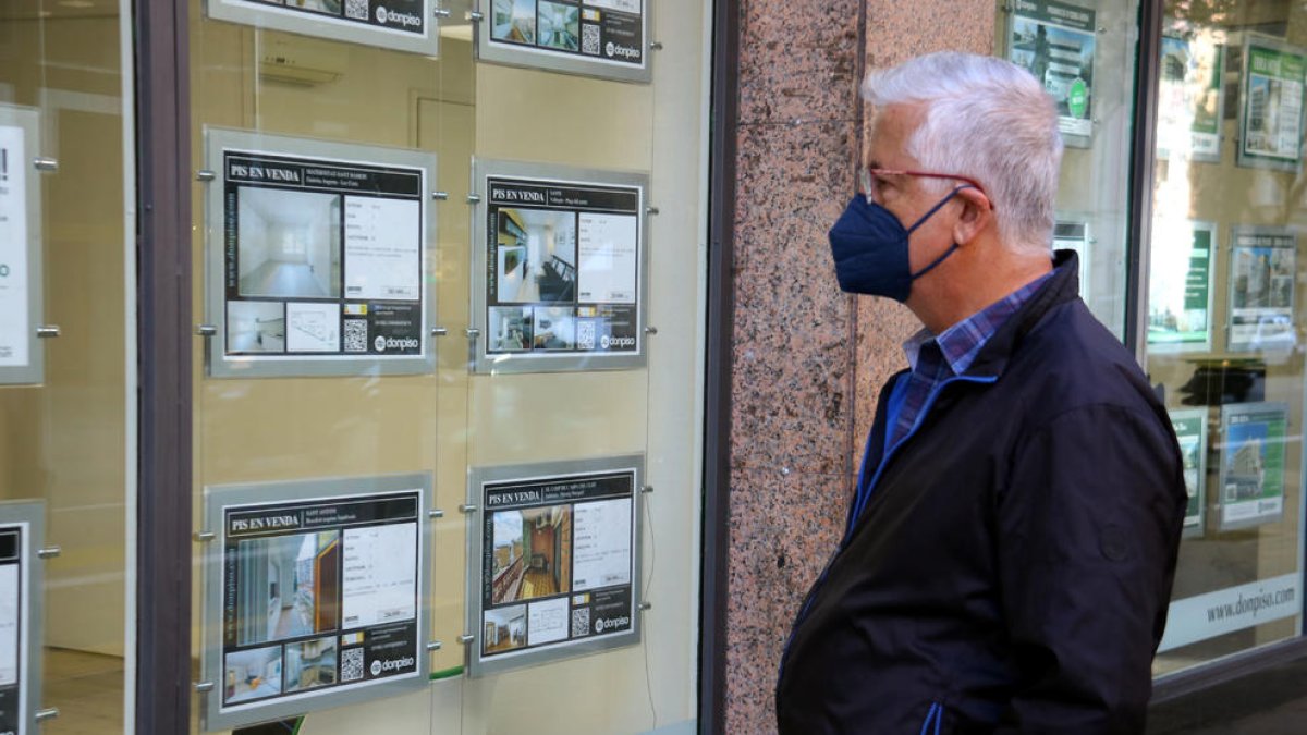 Plano medio de una persona mirando las ofertas de pisos en un escaparate de una inmobiliaria.