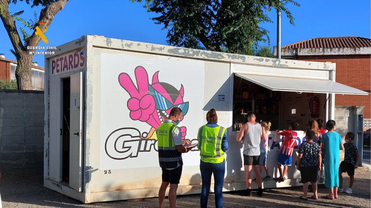 Dos agentes de la Guardia Civil delante de una casita|caseta temporal de venta de petardos donde varios clientes hacen cola.