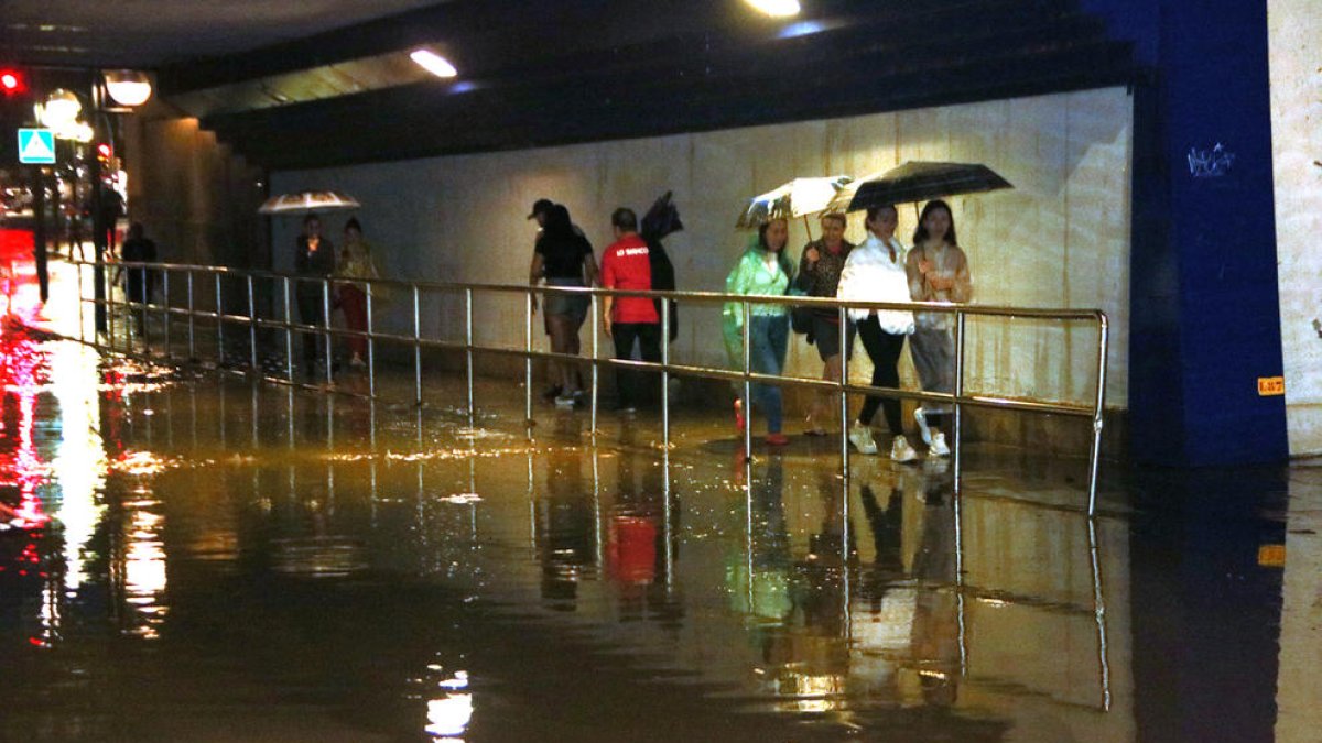 Un grup de persones passa per un pont del barri del Serrallo inundat per la pluja.