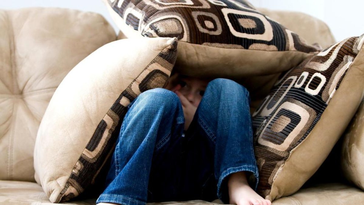 Imatge de recurs d'un nen amagat entre coixins en un sofá.