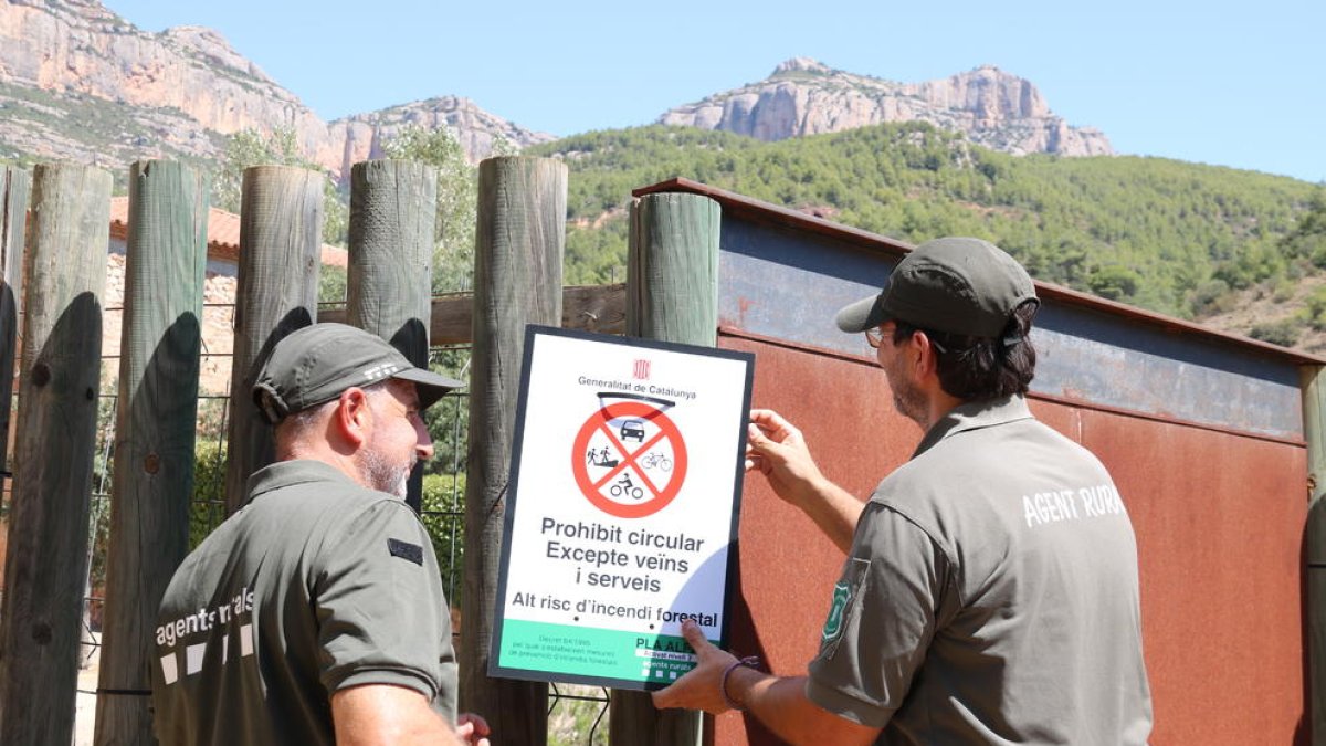 Dos Agents Rurals col·loquen un cartell informatiu a l'accés al Parc Natural de la Serra de Montsant.