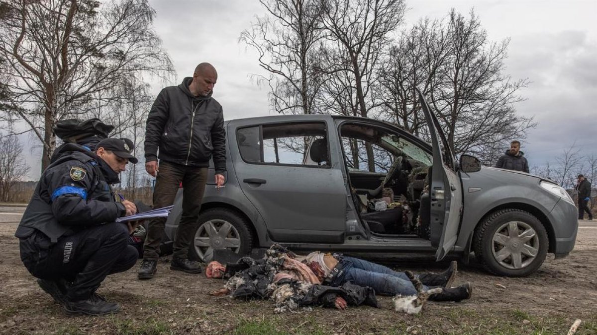 Policies al costat de la dona assassinada estirada a terra al costat d'un cotxe, a Butxa.