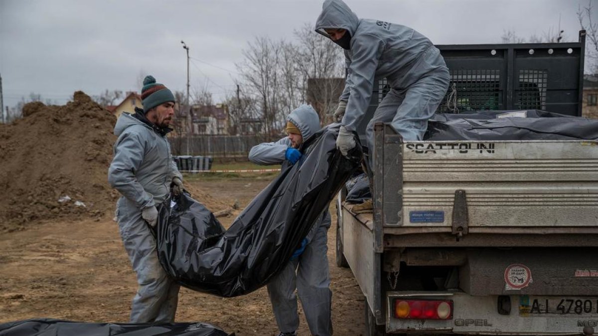 Autoridades forenses recogen cadáveres envueltos en plásticos para su traslado a la morgue, en Bucha.