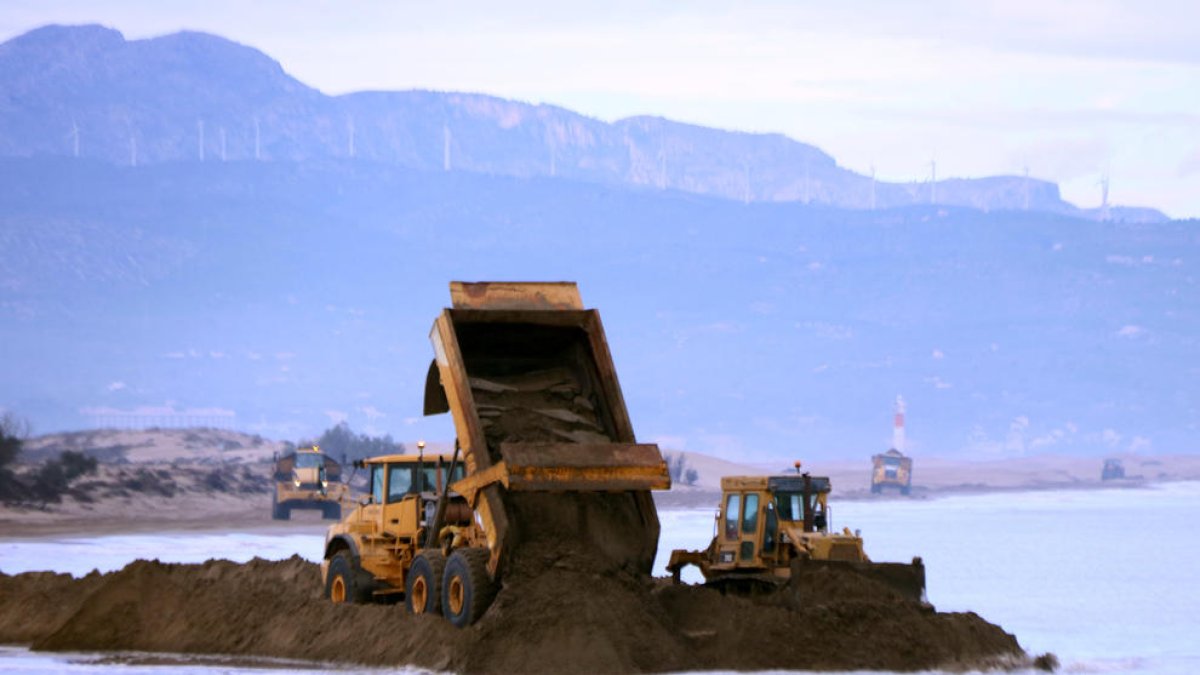 Camiones vertiendo arena y máquinas trabajando en el tramo inicial de la península del Fangar del delta del Ebro.