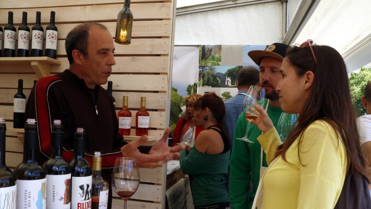 Una chica, con una copa en la mano, escuchando las explicaciones del responsable de una bodega en la Feria del 2019.