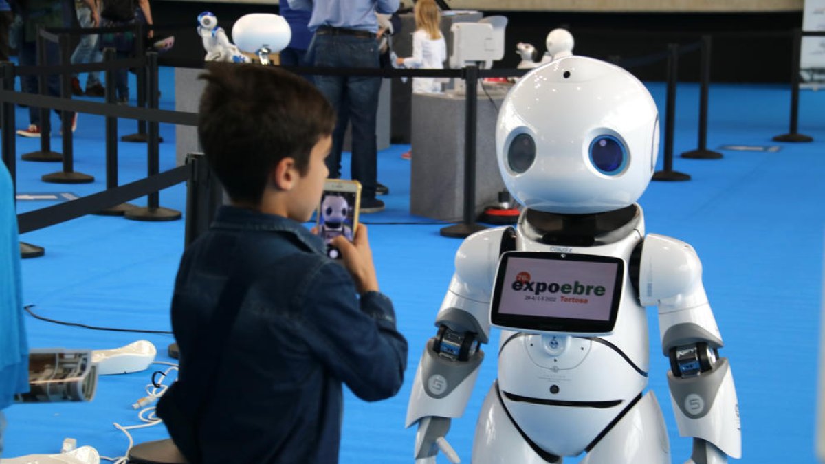 Un niño toma fotos y conversa con un robot humanoide.