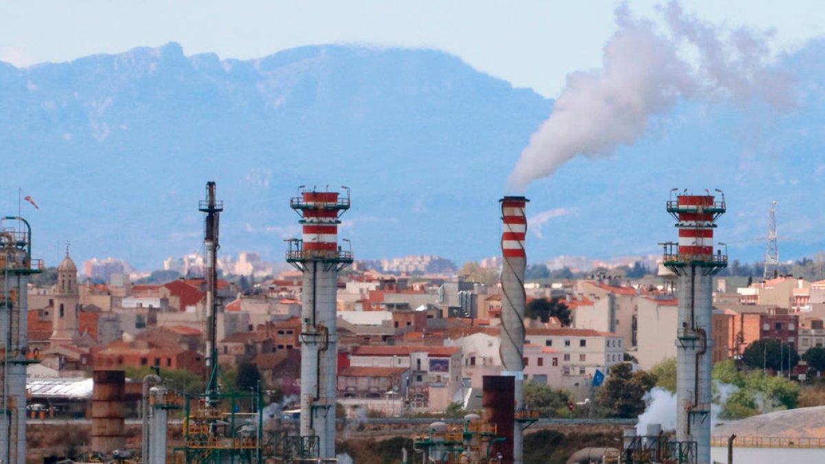 Xemeneies de la indústria química de Tarragona fumejant i, al fons, habitatges dels pobles del Morell i la Pobla de Mafumet.