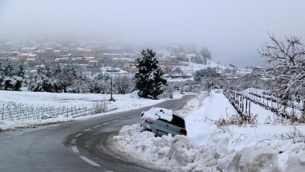 Paisatge nevat a Horta de Sant Joan amb un vehicle que ha sortit de la via a l'entrada al poble.