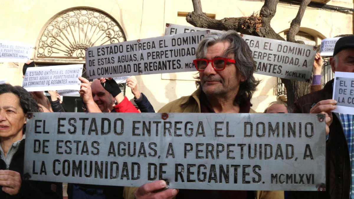 Un home subjectant una rèplica de la placa franquista desapareguda del pantà de Riudecanyes.
