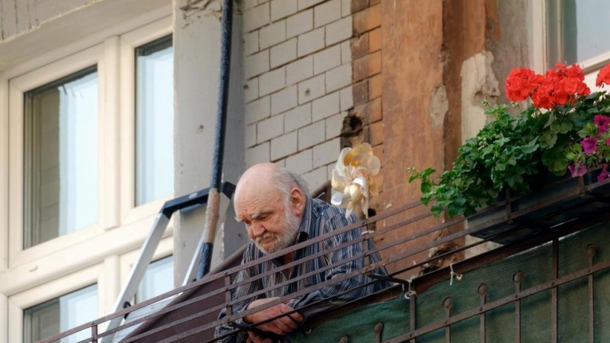 Persona d'edat avançada mirant el carrer des d'un balcó.