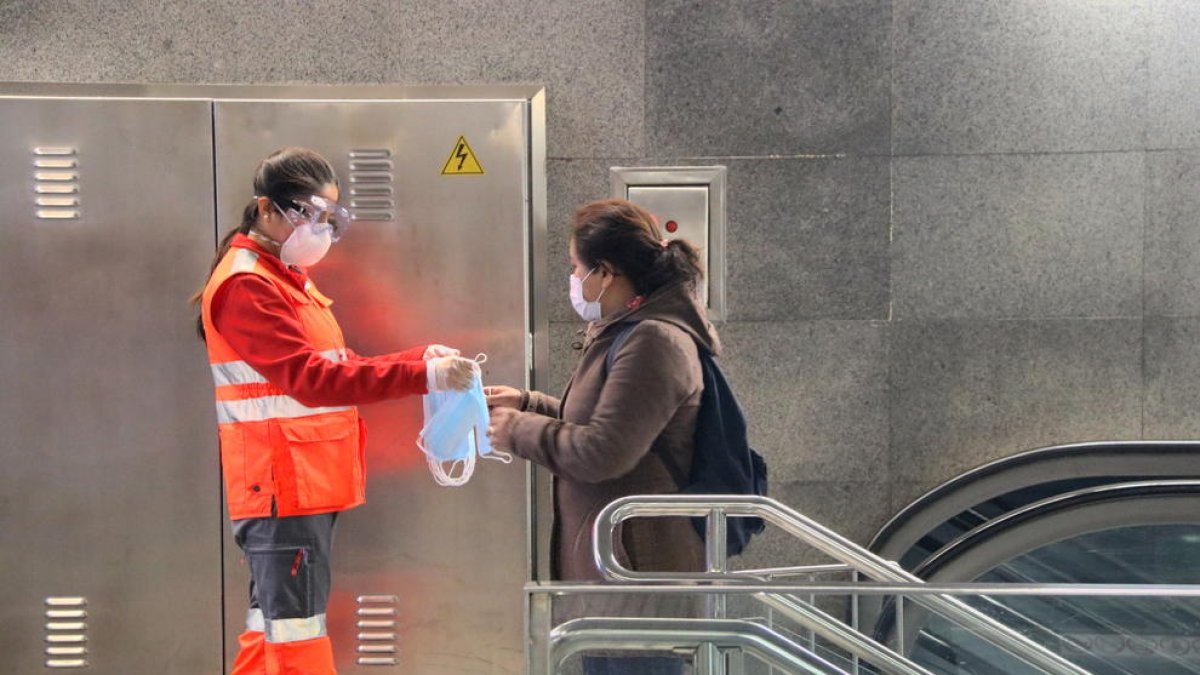 Pla obert d'una voluntària de la Creu Roja entregant una mascareta a l'estació de metro Diagonal de Barcelona.