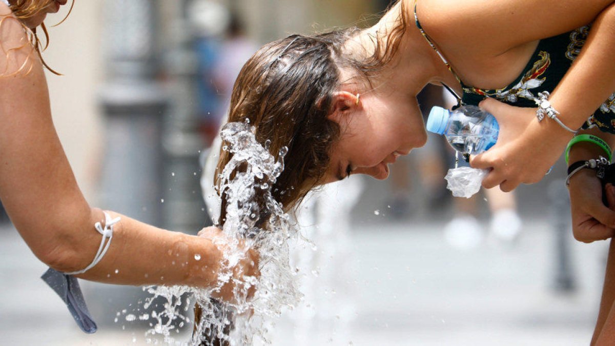 Una mujer se refresca en una fuente para combatir el calor.