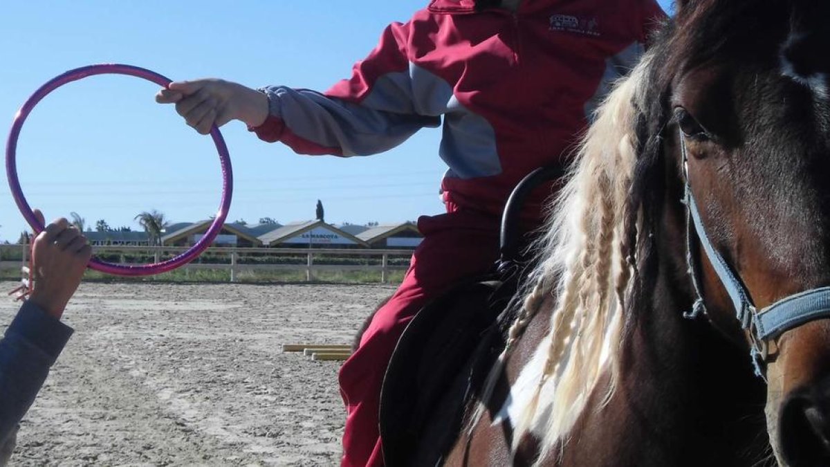 Imatge d'arxiu d'un infant sobre un cavall durant una sessió d'hipoteràpia, amb l'ajuda d'un terapeuta.