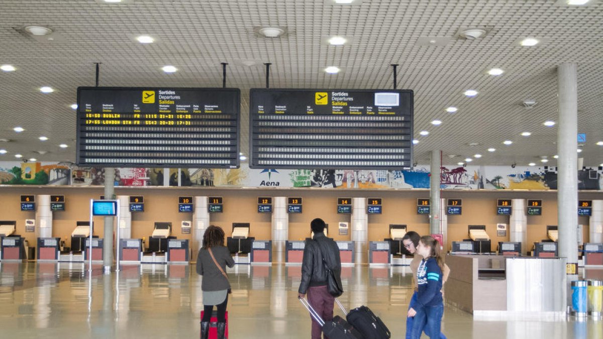 Dos passatgers mirant el tauler de sortides de l'aeroport.