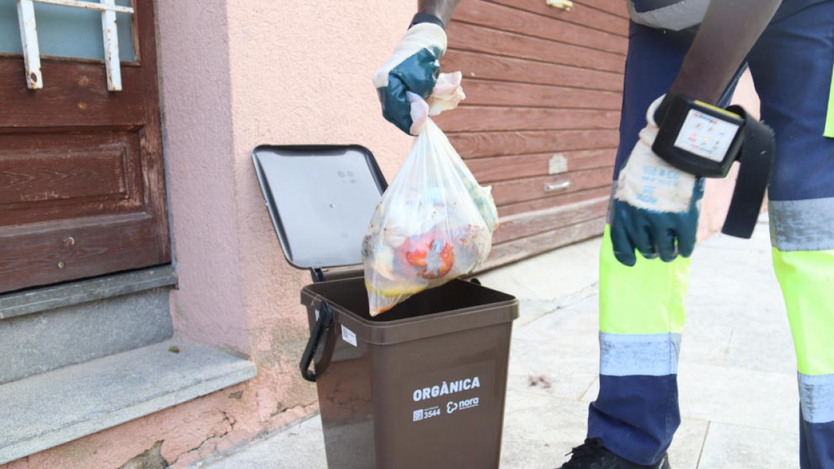 Pla tancat d'un operari traient una bossa d'escombraries del cubell de la fracció orgànica en una recollida porta a porta.