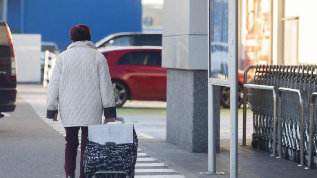 Una mujer sale de un supermercado con la carretilla de comprar.