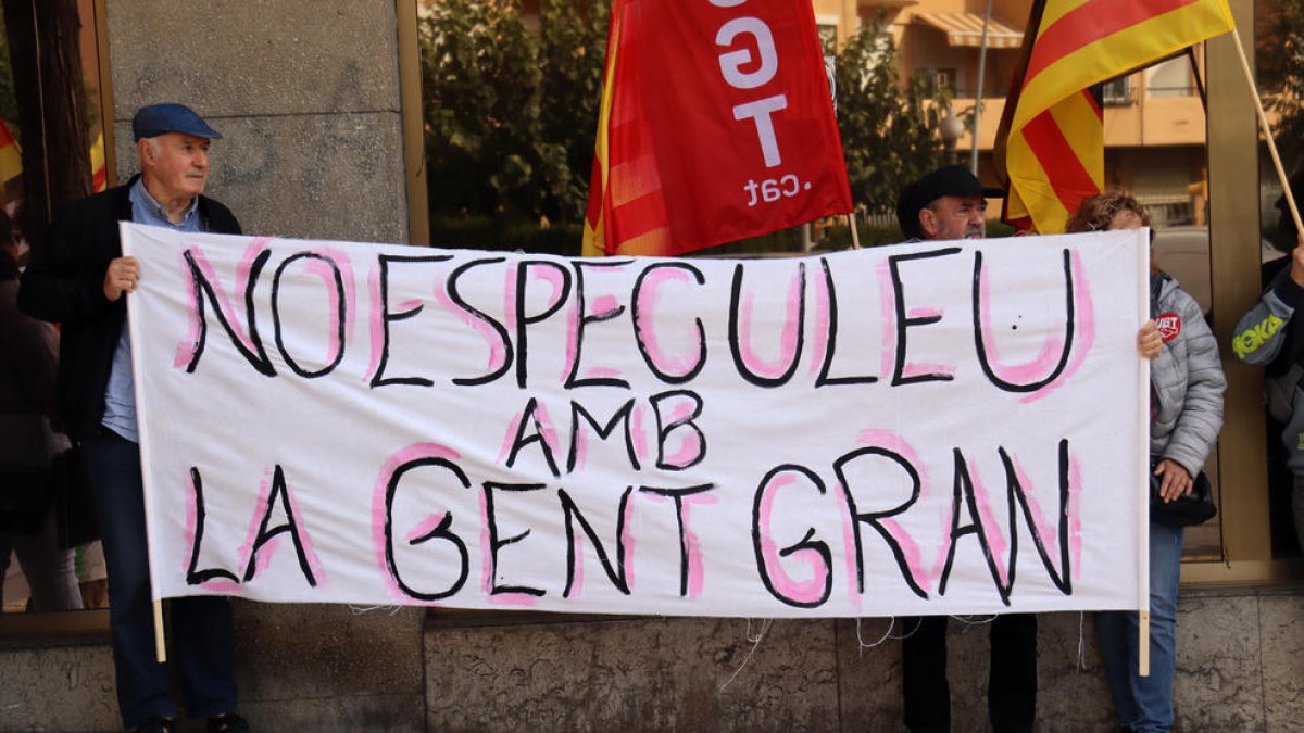 Dues persones subjectant una pancarta durant la concentració que ha tingut lloc aquest divendres davant els serveis territorials de Drets Socials a Tarragona.
