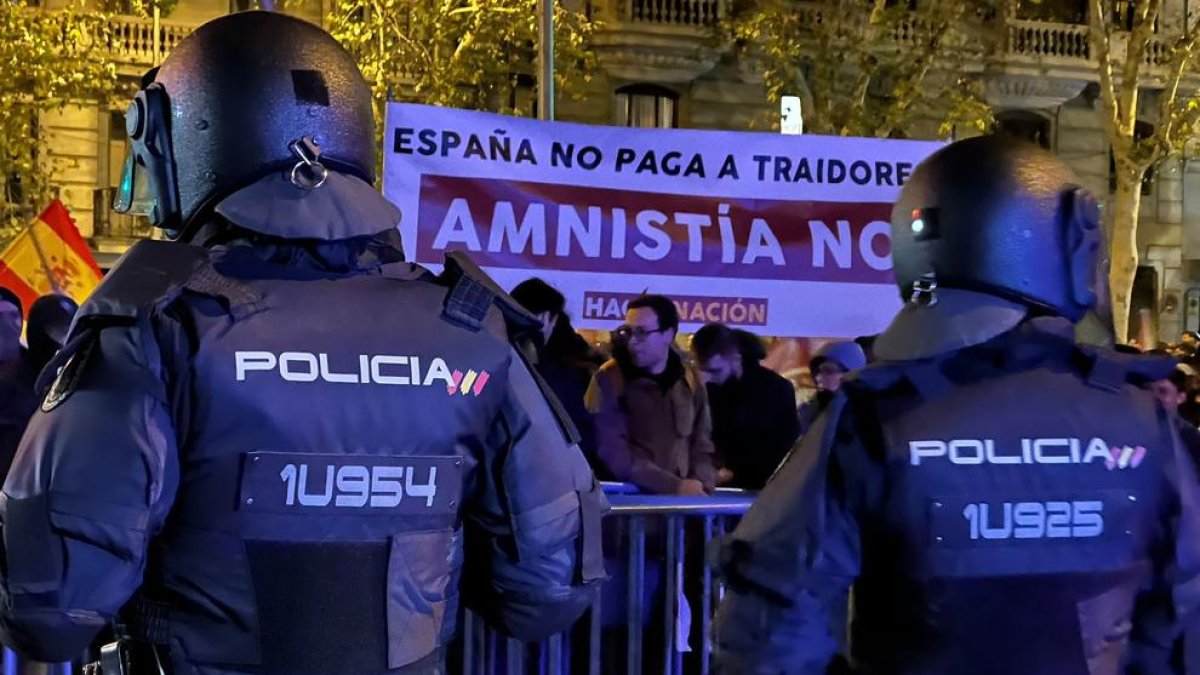 Dos agents de policia custodien la seu del PSOE al carrer Ferraz de Madrid davant de manifestants amb una pancarta contrària a l'amnistia.
