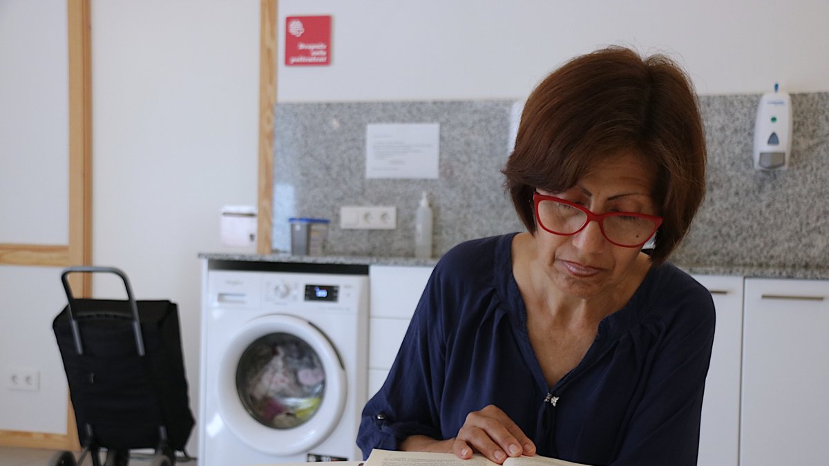 Isabel García, una usuària de Càritas, llegint un llibre mentre espera que acabi la rentadora en un dels punts amb serveis comunitaris de l'entitat