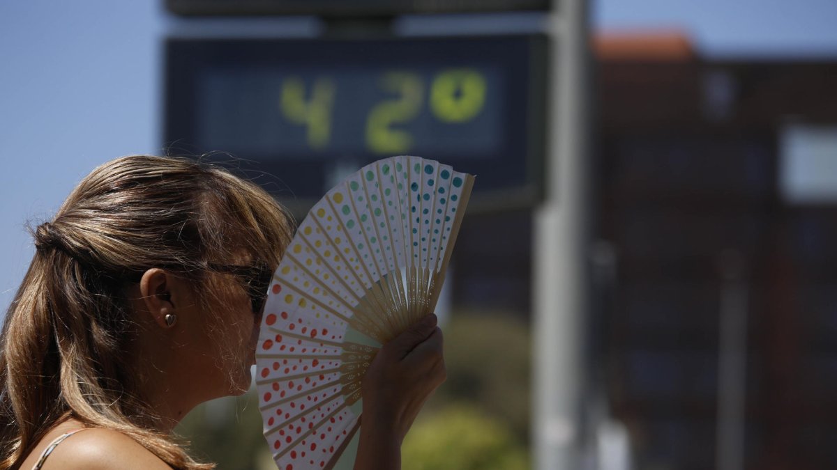 Una mujer se abanica junto a un termómetro de calle que marca 42 grados.