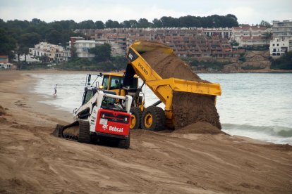 Un camión depositando arena y una excavadora moviendo arena en la playa de Altafulla.