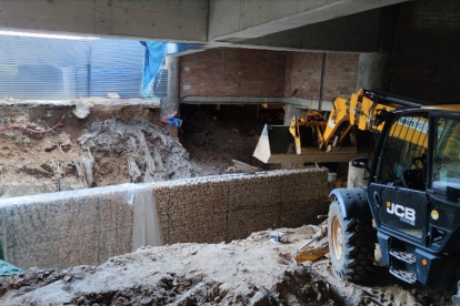 matge de la retroexcavadora a sobre de les restes de la Font dels Lleons, tapada per tones de terra. Al davant, el nou mur de contenció
