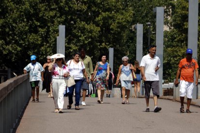 Vianants caminen protegint-se de la calor amb ventalls i gorres.