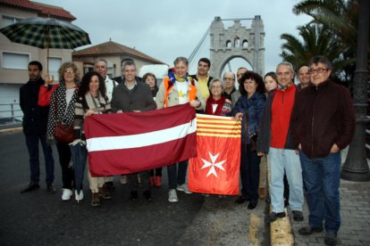 Foto de família del periodista letó Otto Ozols amb representant de l'ANC de les Terres de l'Ebre i de l'Ajuntament d'Amposta davant del Pont Penjant de la capital del Montsià. Imatge del 4 d'abril de 2016