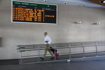 Un home amb una maleta passa per davant del panell que anuncia les sortides a l'estació de Tarragona el 10 de juny de 2016