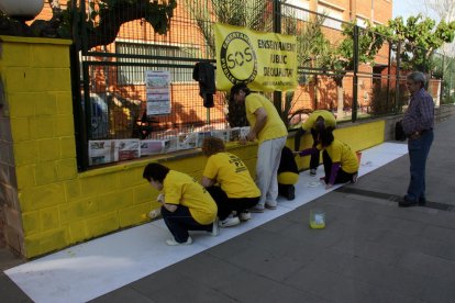 Un grup de mares i pares pintant el mur de l'escola Soriano Montagut d'Amposta. Imatge del 19 d'abril de 2016