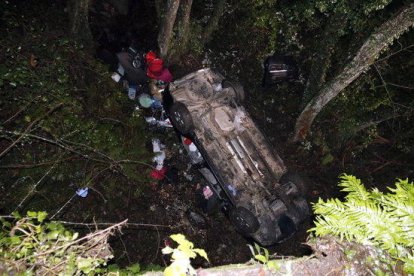 Pla general del cotxe accidentat a Susqueda, cap per avall, amb equips d'emergències treballant.