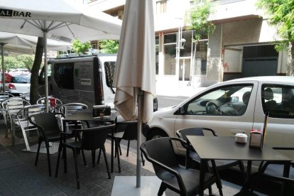 Las mesas y las sillas de la terraza están tocando los vehículos estacionados.