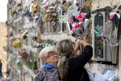 Imagen de dos mujeres poniendo flores en el nicho de un familiar en el cementerio de Montjuïc por Todos los Santos.