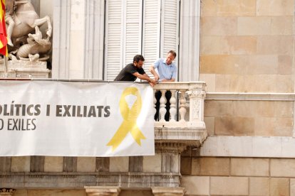 Dos treballadors comencen a treure la pancarta dels presos del Palau de la Generalitat.