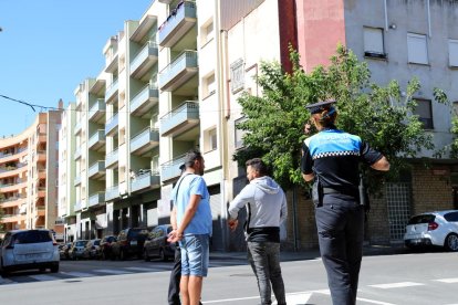 Agents de la Guàrdia Urbana de Reus, en primer terme, conversant amb gitanos que han ocupat un dels pisos, i dalt d'un balcó dels habitatges ocupats, una dona observant-los.