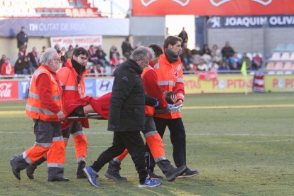 David Querol, amb les mans al cap, acompanyat pel doctor Roca en abandonar la gespa en llitera.