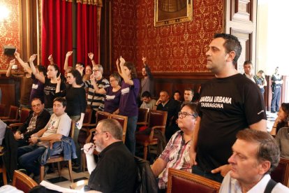 Un agent de la Guàrdia Urbana en primer pla i diversos activistes alçant guixos de color blanc al fons, al ple d'aquest dilluns.