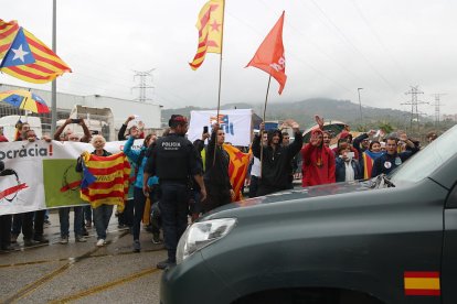 Un vehicle de la Guàrdia Civil marxant de la impremta de Sant Feliu de Llobregat mentre manifestants independentistes exhibeixen estelades i els diuen adéu amb la mà.